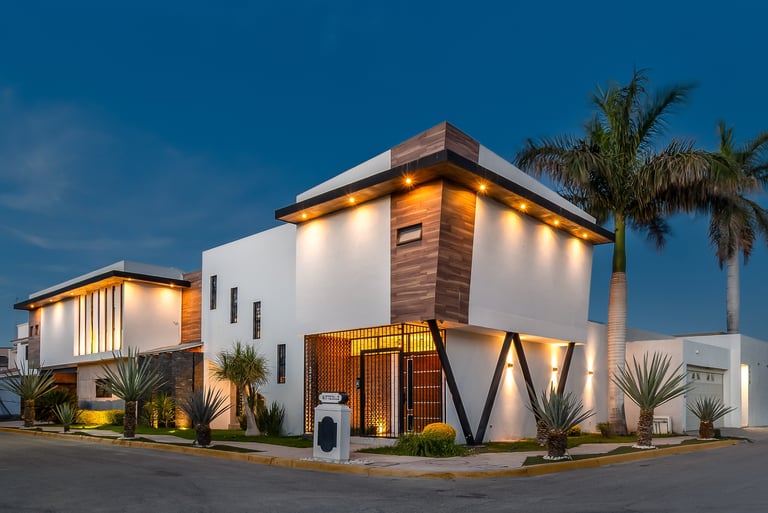 Modern two-story white corner house with warm lighting, wooden accents, and tropical palm trees at dusk