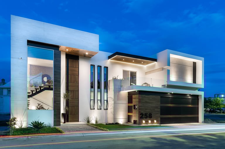 Modern minimalist house with white and black facade, large windows, and dark garage, photographed at dusk against blue sky