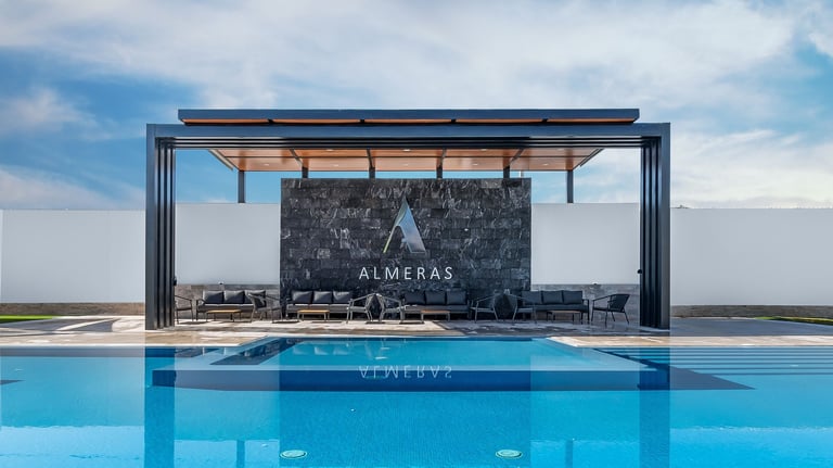 Modern luxury poolside lounge with chalkboard wall, steel pergola, and bright blue swimming pool under cloudy sky