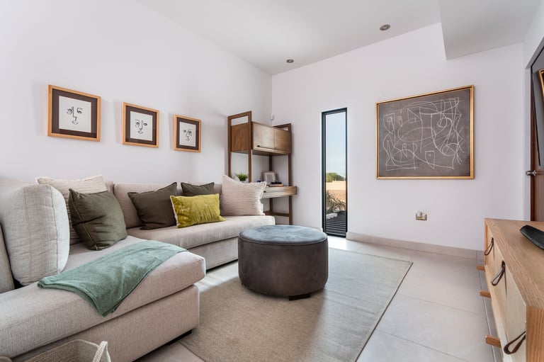 Modern living room with beige L-shaped sofa, wooden frames, dark ottoman, and minimalist decor in neutral tones