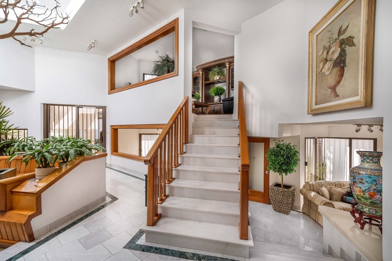 Modern staircase in bright hallway with wooden railings, potted plants, wall art, and shelving with decor