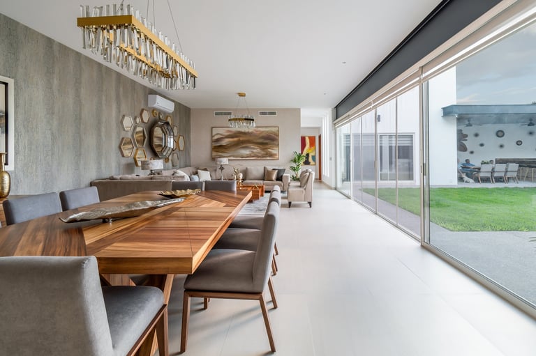 Modern open-concept dining room with wood table, leather chairs, and floor-to-ceiling windows overlooking a green lawn