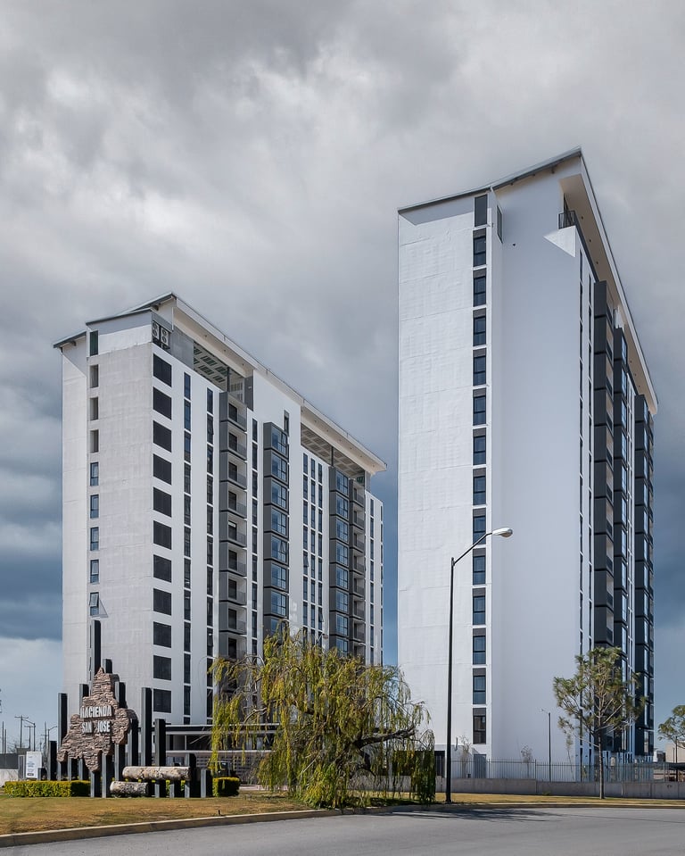 Two modern white residential apartment buildings under cloudy sky with landscaping and street in foreground