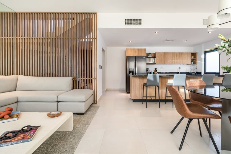 Modern open-plan apartment interior with light beige sofa, wooden kitchen island, dining area, and mid-century modern furnishings