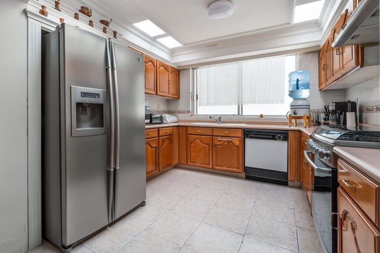 Bright kitchen with stainless steel refrigerator, wooden cabinets, gas range, white tile flooring, and skylight windows