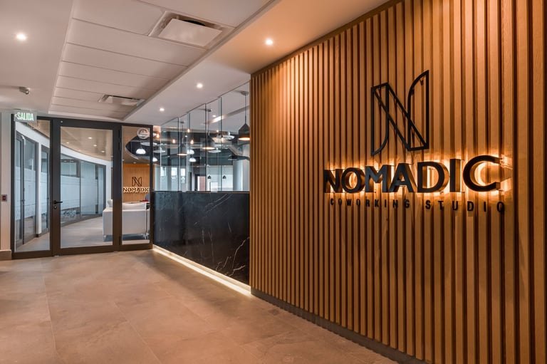 Modern office lobby with Nomadic branding on wooden slat wall and glass-partitioned workspace visible in background