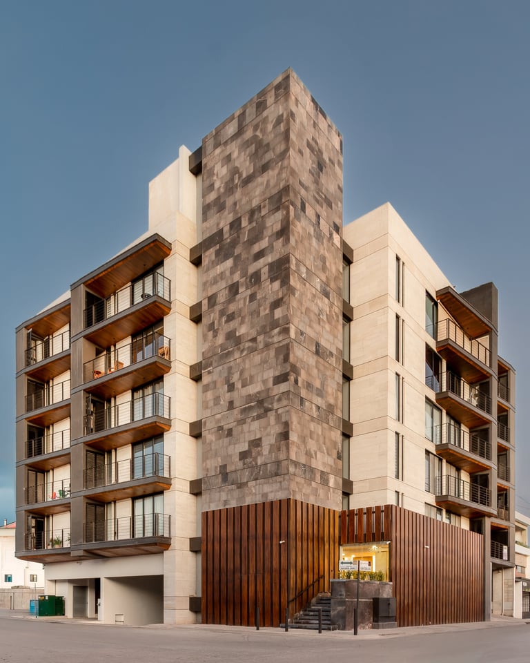 Modern apartment building with mixed materials including cream facade, brown stone tower, wooden balconies, and corrugated metal ground level storefront