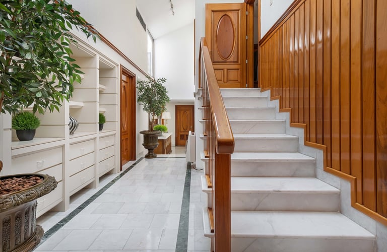 Modern hallway entrance with wooden paneled doors, white built-in shelving with plants, and marble staircase with wooden railings