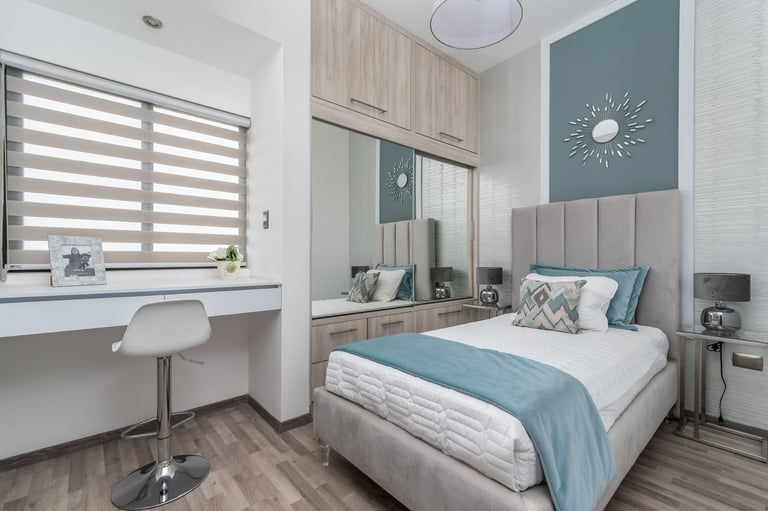 Modern bedroom with teal accents, queen bed with white headboard, desk with striped window blinds, and mirrored wardrobe